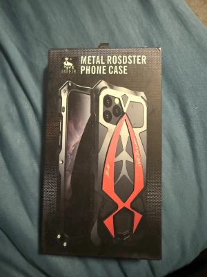 Metallskal GODRIG Metal Rosdster - Snyggt och robust mobilskal i metall från GODRIG, modell Metal Rosdster. Skalets design är svart med röda detaljer och har en futuristisk, kantig form. Passar perfekt för dig som vill ha ett tåligt och unikt skal till din mobil.