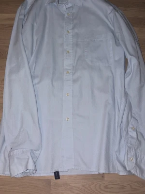 Vit skjorta från Oscar Jacobson - Klassisk vit skjorta från Oscar Jacobson i slim fit-modell. Skjortan har lång ärm, bröstficka och knäppning framtill. Tillverkad i bomull med diskret struktur i tyget. Perfekt för en stilren look.