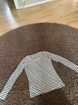 Randig långärmad topp från Lindex - Snygg långärmad topp från Lindex i vitt med svarta horisontella ränder. Tillverkad i mjuk ekologisk bomull och har en klassisk rund halsringning. Perfekt att styla med jeans eller kjol för en enkel och fräsch look.
