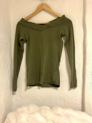 Olivgrön offshoulder långärmad topp - Snygg olivgrön topp med offshoulder-design och lång ärm. Toppens form är slim och den har en v-ringad form. Nypris 450kr, nästan aldrig använd🤗