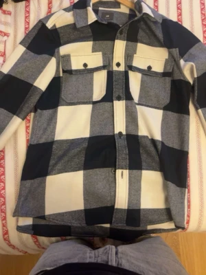 Rutig overshirt HM - Stilren overshirt från H&M i stora blå och vita rutor. Skjortan har två bröstfickor med lock och knappar framtill. Perfekt att bära öppen eller stängd för en avslappnad look. Tillverkad i mjuk bomull och har lång ärm.