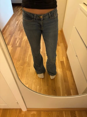 Blå bootcut jeans från Vero Moda - Säljer ett par klassiska blå bootcut jeans från Vero Moda. Jeansen har låg/mid midja, fem fickor och stängs med knapp och dragkedja. Tillverkade i denim med snygga sömmar och lätt utsvängda ben. Perfekta för en avslappnad och trendig look. Lite slitna nere vid benen, de är lite lite långa för mig som är 156cm. Annars inga defekter. Jättesköna jeans som knappt känns som jeans och stretchiga🦋💙
