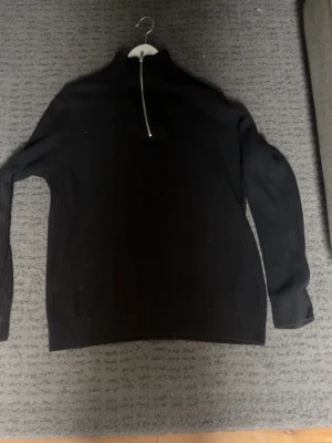 Svart stickad tröja med halvzip - Snygg svart stickad tröja från Jack & Jones med halvzip och hög krage. Tröjan har långa ärmar och ribbade muddar vid ärmslut och nederkant. Perfekt för lager på lager och enkel att matcha med olika outfits. Passar dig som är 170-180cm storlek S står i den men sitter som M