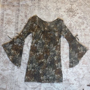 Leopardmönstrad klänning med trumpetärm - Cool leopardmönstrad klänning med trumpetärmar och knytdetaljer på ärmarna. Klänningen har en lös passform och är perfekt för dig som gillar att sticka ut. Materialet känns lätt och luftigt, och färgerna går i brunt, beige och svart.