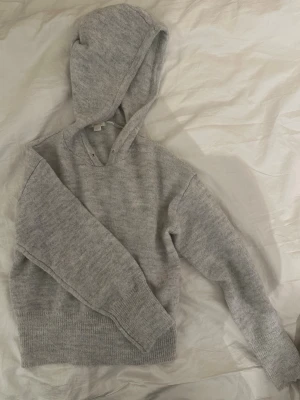 Grå stickad tjocktröja - Mysig grå stickad hoodie med luva och långa ärmar. Tröjan har bred ribbstickad mudd vid midjan och ärmarna, samt en avslappnad passform. Perfekt för lager på lager och chill dagar.