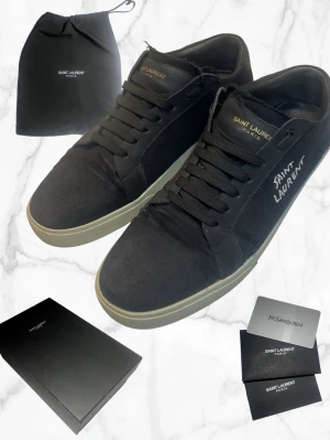 Saint Laurent skor - Snygga svarta sneakers från Saint Laurent i canvasmaterial med vita detaljer och logga på sidan samt plösen. Klassisk låg modell med svarta skosnören och vitgul sula. Perfekta för dig som gillar stilrena och exklusiva sneakers.