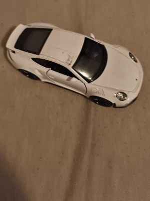 Vit leksaksbil Porsche - Säljer en vit leksaksbil som liknar en Porsche med svarta detaljer och sportig design. Bilen har tydliga dörrlinjer, svarta fönster och realistiska strålkastare. Perfekt för dig som gillar bilar och samlar på modellbilar.