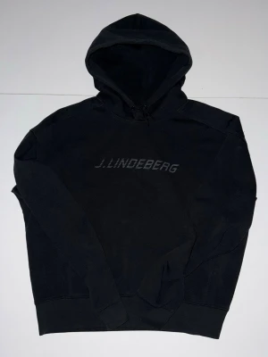 J.Lindeberg Svart Hoodie - Stilren svart hoodie från J.Lindeberg med diskret logga framtill och liten JL-detalj på ryggen. Perfekt för en avslappnad och trendig look. Den är i storleken M men modellen är mer som S skulle jag säga.