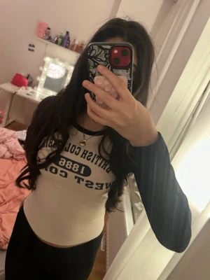 Ribbad långärmad topp British Columbia - Trendig ribbad långärmad topp med svart text 'British Columbia 1886 West Coast' på bröstet. Toppen har kontrastfärgade svarta ärmar och vit kropp, samt rund halsringning. Perfekt för en avslappnad och sportig look.