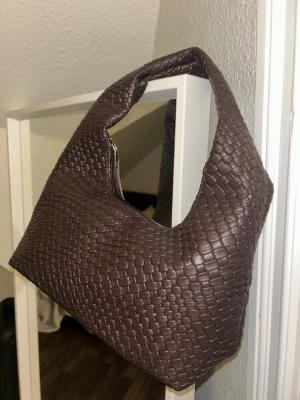 Brun flätad axelväska - Säljer en brun handväska med flätad design köpt utomlands i Spanien förra året. Den är aldrig använd och har inga defekter🩷