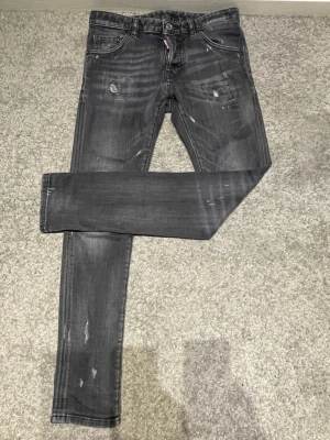 Grå slitna skinny jeans Dsquared2 - Säljer ett par grå skinny jeans från Dsquared2 med slitningar och distressed detaljer. Jeansen har fem fickor, knappgylf och en cool tvättad look. Perfekta för dig som gillar streetwear och vill ha en edgy stil. Knappt använda 