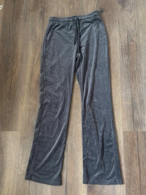 Grå mjukisbyxor i velour - Säljer ett par grå mjukisbyxor i mjuk velour med raka ben och dragsko i midjan. Perfekta för chill dagar och har en skön, avslappnad passform. Inga synliga loggor eller fickor. Passar dig som gillar en enkel och stilren look.