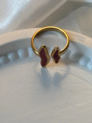 Guldfärgad ring med röd emalj - Unik guldpläterad ring med två abstrakta former i röd emalj på öppningen. Ringen har en modern och trendig design som sticker ut och passar perfekt för dig som gillar unika smycken. 