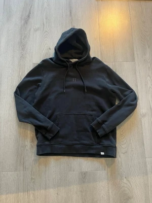 Les duex  - Snygg svart hoodie från Les Deux med minimalistisk design och broderad II-logga på bröstet. Hoodien har justerbar dragsko i huvan och en klassisk magficka. Tillverkad i mjukt bomullsmaterial som känns skönt mot huden. 