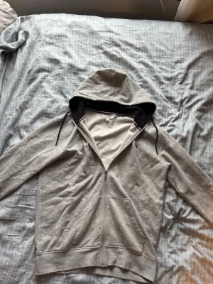 Grå hoodie från Us Polo Assn - Snygg grå hoodie från Us Polo Assn med svart broderad logga på bröstet. Hoodien har dragkedja, snörning i huvan och två stora fickor framtill. Insidan av huvan är svart för en schysst kontrast. Perfekt till chill vardagsstil. Är inte använd alls eftersom den var för stor och är helt ny utan några fel eller skador. Tröjan är i storlek M. Köpt från deras officiella hemsida (Nypris 700kr)