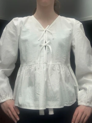 Vit blus med rosetter - Vit blus med två små rosetter vid bröstet. Blusen är från Gina Young. Den är väldigt fin, något kort i armarna men inget som stör mig så mycket. Den är lite genomskinlig i ryggen, vill man ha bild kan man kontakta mig så fixar jag!🩷 Använd en gång så den är i väldigt bra skick! 