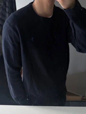 Mörkblå tröja från Polo Ralph Lauren - Klassisk mörkblå tröja från Polo Ralph Lauren med rund halsringning och diskret broderad logga på bröstet. Tillverkad i mjuk bomull och har ribbade muddar vid ärmslut och nederkant. Perfekt för en stilren och enkel look. Storlek xl för barn så sitter som S 