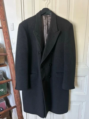 Vintage dubbelknäppt rock  - En vintage dubbelknäppt rock. Gjord av 80% ull och 20% kashmir. Färgen är mörkgrå/svart och rocken är i mycket fint skick.