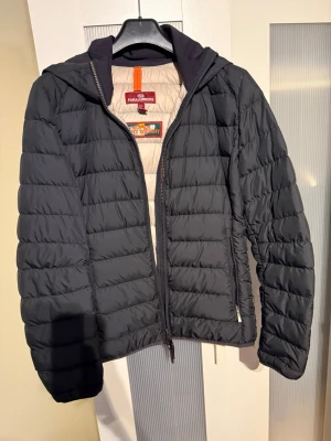 Mörkblå dunjacka från Parajumpers - Snygg mörkblå  dunjacka från Parajumpers med quiltad design och huva. Jackan har dragkedja framtill och ljus insida med märkets logga. Tillverkad i superlätt material som håller dig varm under kalla dagar. Perfekt för dig som vill ha både stil och funktion.