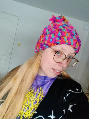 Färgglad virkad mössa med tofs hippie boho  - Säljer en handvirkad mössa i chunky garn med massor av färger som rosa, blå, gul och lila. Mössan har en stor tofs på toppen och är riktigt mjuk och varm. Perfekt för dig som vill sticka ut med en unik accessoar!