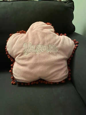 Bratz kudde - Unik blomformad/stjärnformad kudde i mjuk rosa plysch med vinröda bollar längs kanten. Ena sidan har broderad Bratz-figur och logga, andra sidan har texten 'Yasmin' broderad. Perfekt som dekoration eller mysig detalj i soffan eller sängen.