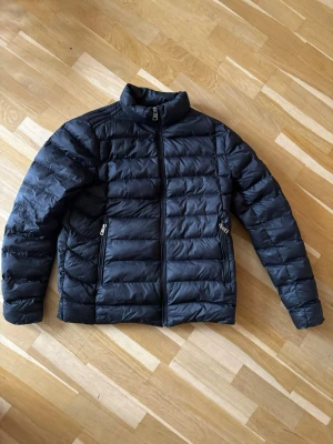 Moncler Jacka - Snygg svart pufferjacka från Moncler med hög krage och två framfickor med dragkedja. Jackan har quiltad design med horisontella sömmar och stängs med dragkedja framtill. Perfekt för våren den ger en clean look. Jackan är äckta och i fin kvalité. Inge defekter. Priset är ej hugget i sten! Tveka inte om att höra av er😊