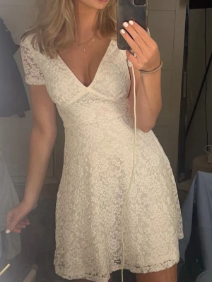 Vit spetsklänning med v-ringning - Säljer en vit kortklänning med v-ringad hals och spetsdetaljer. Klänningen har korta ärmar och ett feminint snitt som framhäver figuren. Perfekt för sommarens alla tillfällen, och den är gjord i ett lätt och luftigt material. Använd en gång!