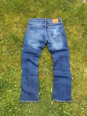 Levis 527 jeans bootcut  - Klassiska blå jeans från Levi's med bootcut. Jeansen har två bakfickor och detaljer i… brunt lädermärke briefly bak. Perfekta för dig som gillar tidlös denimstil.