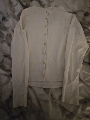 Beige tunn kofta med knappar - Stilren beige kofta med rund halsringning och knäppning framtill. Långärmad modell i tunt, mjukt material som passar perfekt för lager på lager. Diskret liten logga nertill. Enkel att matcha till olika outfits.