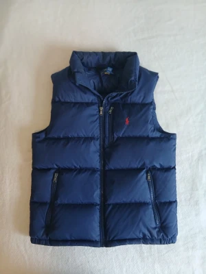 Mörkblå Dunväst från Polo Ralph Lauren - Hej!! Säljer en otroligt snygg och stilren väst från Polo Ralph Lauren perfekt för tider som denna! Nypris är runt 2900 sek tror jag och den är i väldigt bra skick. Den är även väldigt skön att ha på sig och passar bra till alla tillfällen. Storlek 14-16 L så skriv gärna om ni vill ha en bild hur den sitter eller om ni har någon fråga. Pris kan såklart diskuteras plus att det är frifrakt!:)