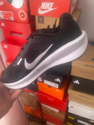 Svarta Nike sneakers med vit sula - Snygga svarta Nike sneakers med vit sula och stor vit Swoosh-logga på sidan. Ovandelen är i meshmaterial för bra andningsförmåga och skon har klassisk snörning. Perfekt för dig som gillar sportig och stilren look.