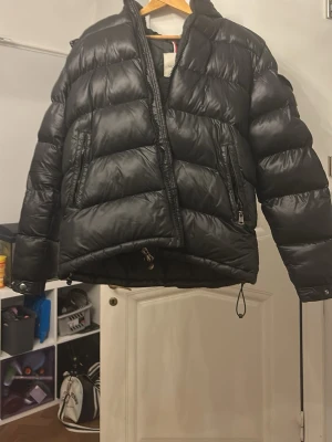 Svart pufferjacka från Moncler - Säljer en svart pufferjacka från Moncler med klassisk logga på ärmen. Jackan har två snedställda dragkedjefickor fram, hög krage och dragsko i nederkant. Materialet är glansigt och quiltat, perfekt för kalla vinterdagar. Den är äkta. 20.000kr❌         4000kr✅