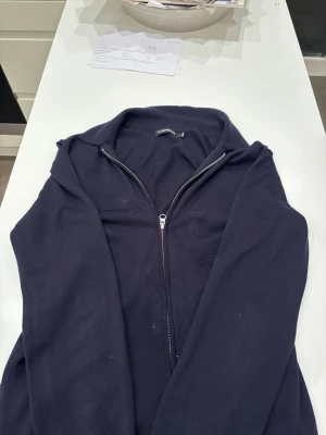 Mörkblå stickad helzip från J Lindeberg  - Mörkblå stickad tröja med dragkedja framtill och krage. Väldigt bra skick och en mycket fet tröja som nästan passar till allt! Säljer till ett mycket bra pris och kontakta mig för mer!😁