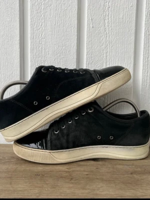 Lanvin skor  - Lanvin skor i storlek 6 (motsvarar ca 40-41). Skick 6,5-7/10 med tydligt användningstecken men fortfarande bra helhetsintryck. Ena skon har en repa i glansen där översta lacklagret släppt (se bild 3). Sulan är något nedsliten, mockan har tappat lite färg på vissa ställen, normal slitage efter mycket användning. I övrigt bra skick och mycket kvar att ge. Endast skor samt dustbag ingår. Nypris cirka 4 000-6 000 kr | Vårt pris 1800kr.