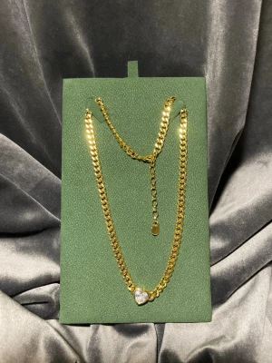 Guldigt halsband med hjärthänge - Snyggt halsband i guldplätera i rostfritt stål med en chunky kedja och ett gnistrande hjärthänge framtill. Hjärtat är dekorerat med en klar sten som ger extra bling. Justerbar längd med förlängningskedja. Perfekt för dig som gillar statement-smycken.