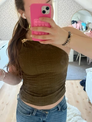 Olivgrön oneshoulder topp - Säljer en olivgrön oneshoulder topp med snyggt axelband i metall. Toppen är croppad och har en tight passform som framhäver figuren. Från hm i storlek S, använd ca två gånger. Så fin färg och snygg för sommaren!🩷🩷