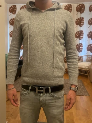 Drakenberg-Merinoull hoodie  - Snygg ljusgrå hoodie med huva och långa dragskor. Tillverkad i mjukt, stickat material som känns riktigt skönt mot huden. Klassisk passform medi ribbade muddar vid ärmslut och nederkant. Perfekt för dig som gillar en clean och stilren look.