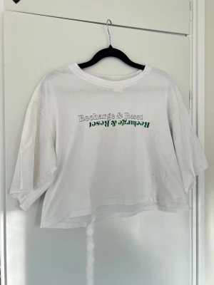 Croppad oversized t-shirt med tryck, stl S - En vit croppad t-shirt med tryck från H&M i storlek S. Sparsamt använd. Har två små prickar på framsidan som inte verkar gå bort i tvätten. Lite oversized. Tvättlappen finns ej kvar. 