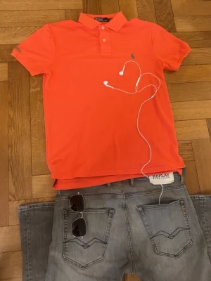 Polo by Ralph Lauren piké  - Grym kvalité, inga defekter. Storlek S, sitter bra vid axlarna och slutar vid midjan. Bilderna kan va missledande, färgen är mer rosa än orange, men den är koral färgad.   Mått -|-  Axelmått: 42 cm  Längd: 64 cm  Bröst: 46 cm   Leverans sker dagen efter, har du nån fråga är det bara att skriva:) 