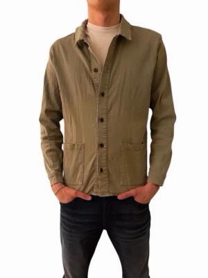Olivgrön overshirt med fickor - Stilren olivgrön overshirt med raka linjer och två stora framfickor. Skjortjackan har knäppning framtill med mörka knappar och klassisk krage. Tillverkad i ett mjukt bomullstyg som ger en avslappnad look. Perfekt att bära över en t-shirt för en casual stil.