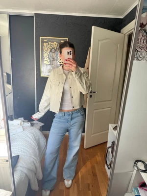 Beige cropped skinnjacka - Säljer en beige lite cropped jeansjacka med raka axlar och klassisk krage. Jackan har två bröstfickor med lock och knappar framtill. 