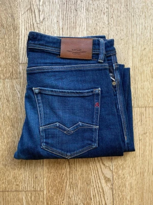 Mörkblå jeans från Replay w32 L34 - Snygga mörkblå jeans från Replay med klassisk femficksmodell och detaljerade sömmar på bakfickan. Jeansen har en skinnpatch med logga bak i midjan och är tillverkade i mjukt denimtyg. Perfekta för en avslappnad men stilren look.