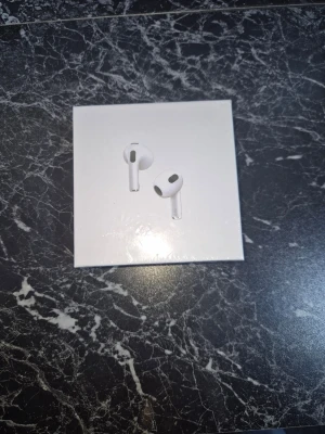 Apple AirPods 3 trådlösa hörlurar - Säljer ett par vita Apple AirPods 3 med laddningsetui. Hörlurarna har en stilren och modern design med rundade former och sitter bekvämt i öronen. Perfekta för musik, samtal och träning. Kommer i originalförpackning. BEHÖVER LADDAS!!!