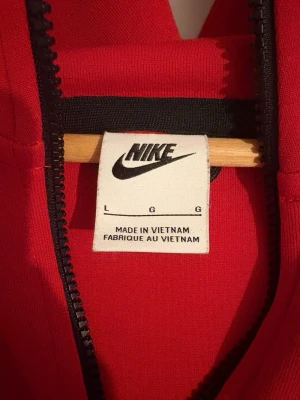 Röd Nike Tech - Säljer en snygg röd hoodie från Nike i storlek L. Den har en dragkedja framtill och en praktisk ficka på ärmen. Perfekt för höst och vår, med en sportig look och bekväm passform. Huvan ger extra värme och stil. Passar både till träning och vardag! Priset kan diskuteras 