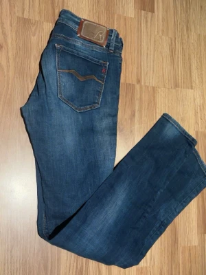 Blå jeans från Replay med slitningar - Säljer ett par feta blå jeans från Replay med slitningar och distressed detaljer på benen. Jeansen har klassisk femficksmodell, smal/anbass lik passform och snygga kontrastsömmar. Perfekta för en avslappnad och trendig look.