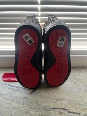 Louboutin - Snygga svarta sneakers från Christian Louboutin med klassisk röd sula och svart ovandel i mocka. Skorna har svarta skosnören och en låg profil som ger en clean och stilren look. Perfekta för dig som vill ha något exklusivt och trendigt.