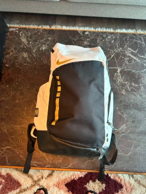 Nike elite backpack - ryggsäck från Nike i vitt med guld. Stor framficka med dragkedja, justerbara och vadderade axelband med transparenta detaljer. Perfekt för skolan eller träningen, med klassisk Nike-logga på både fram- och baksida. Tillverkad i slitstarkt syntetmaterial.