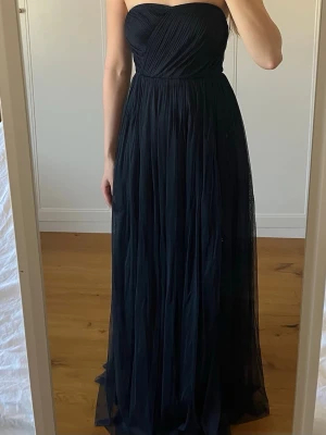 Marinblå axelbandslös balklänning - Elegant marinblå långklänning med axelbandslös design och draperad överdel. Kjolen är luftig och faller snyggt i flera lager. Perfekt för bal eller festligare tillfällen. Endast använd en gång, nypris va ca 1200