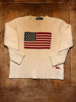 Stickad Ralph Lauren tröja - Ralph Lauren vit lammulströja med USA motiv. Tröjan är genuint en av de finast stickade tröjorna jag har sett, materialet är av högsta kvalitet. Tröjan är av tjock lammull. Storleken är L men i och med att det är en Unisex tröja är storleken närmare L för tjejer och M/S för killar. Hör av dig vid frågor eller prisförslag!