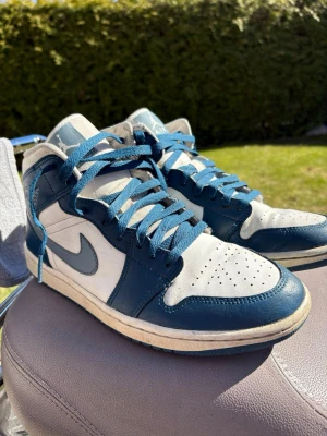Nike Air Jordan 1 blå/vita sneakers - Snygga Nike Air Jordan sneakers i blått och vitt med klassisk siluett. Skorna har blå snörning, perforerad tåbox och ikoniska swoosh-loggan på sidan. Tillverkade i skinn med kontrasterande färgblock och retro vibe. Perfekta för dig som gillar streetwear och sportig stil. Pris kan diskuteras!